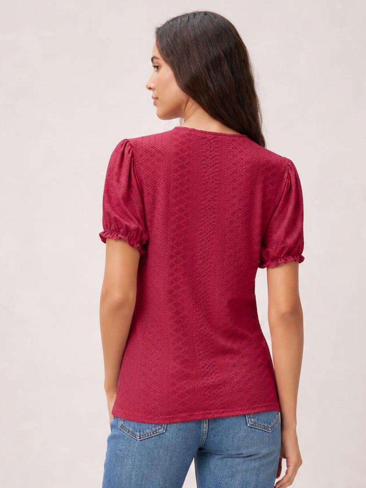 A model wears a burgundy eyelet blouse with a round neck, short puff sleeves, delicate frill cuffs, and a fitted silhouette, shown from the back.