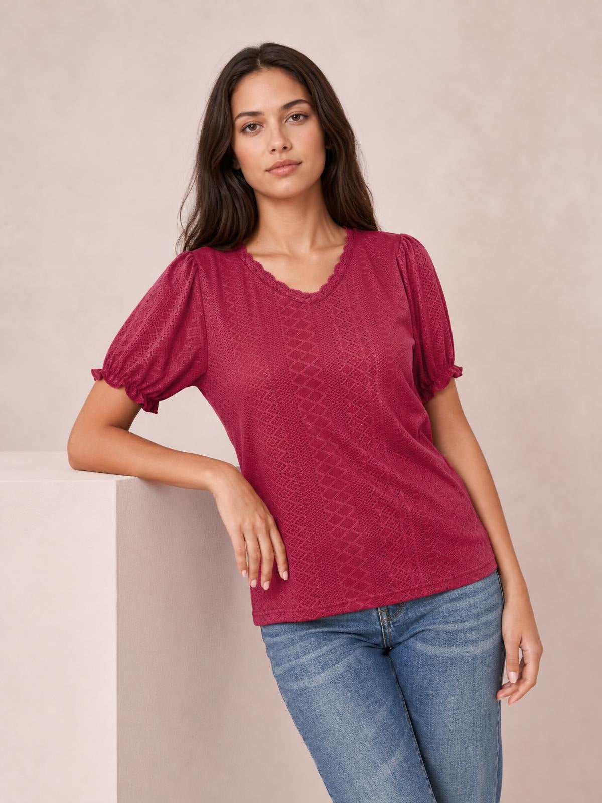 A model leans on a block wearing a burgundy eyelet blouse with a delicate frill-trimmed neckline, short puff sleeves, and a relaxed straight silhouette.