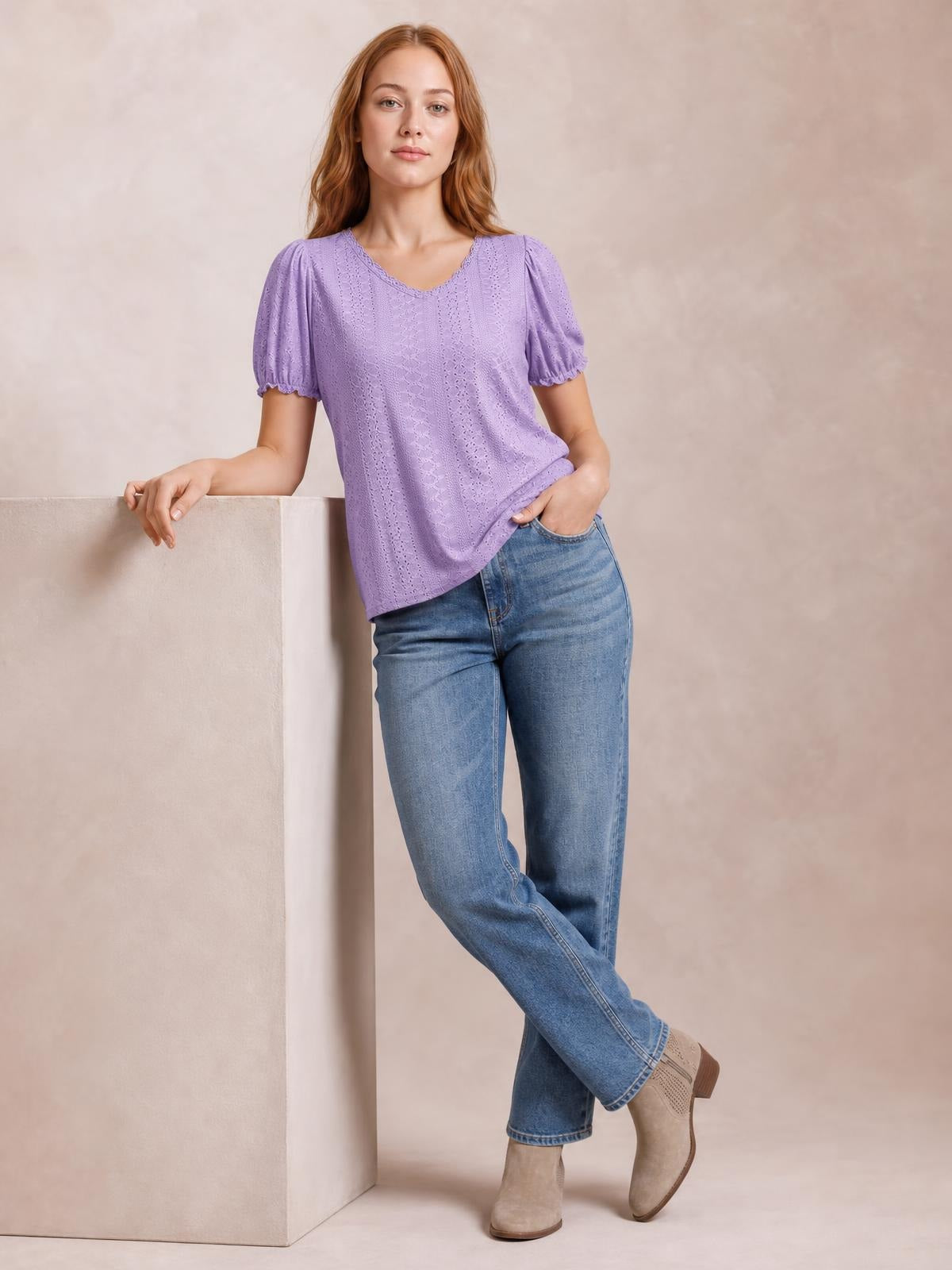 A model wears a lavender eyelet blouse with a round neckline, short puff sleeves, delicate frill trim, and a relaxed silhouette while leaning casually.