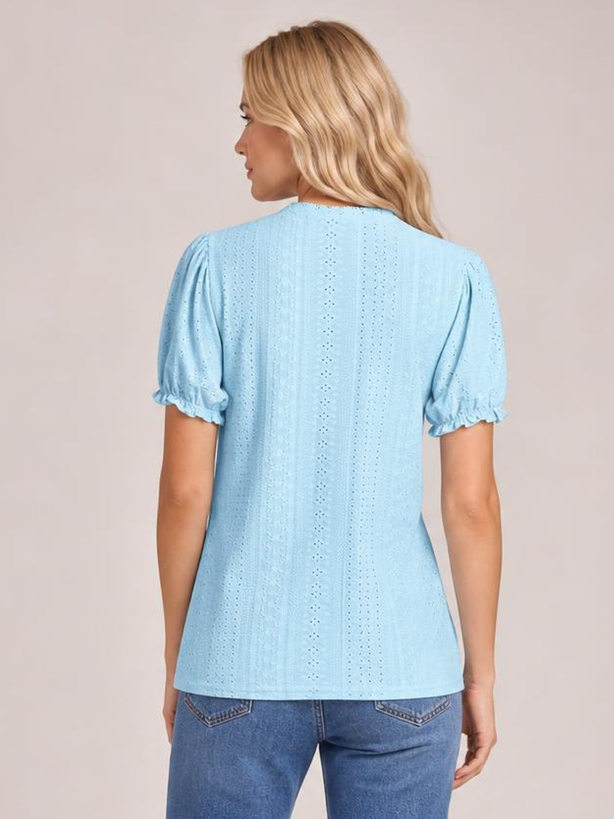 Model shown from the back in a light blue eyelet blouse with a round neck, short puff sleeves, delicate frilled cuffs, and a straight silhouette.