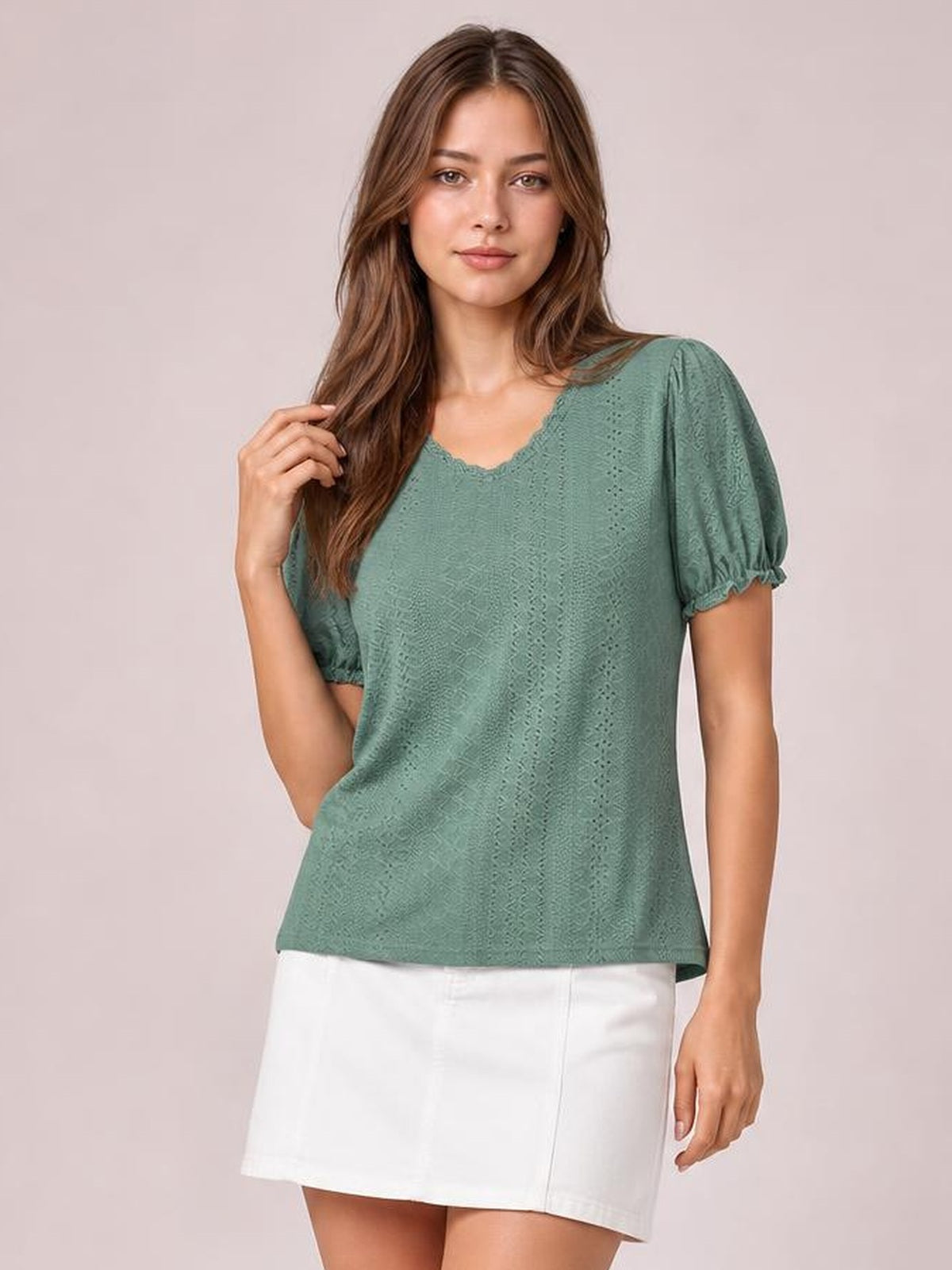 A model poses in a sage-green eyelet blouse with a round frilled neckline, short puff sleeves with elastic cuffs, and a relaxed straight silhouette.