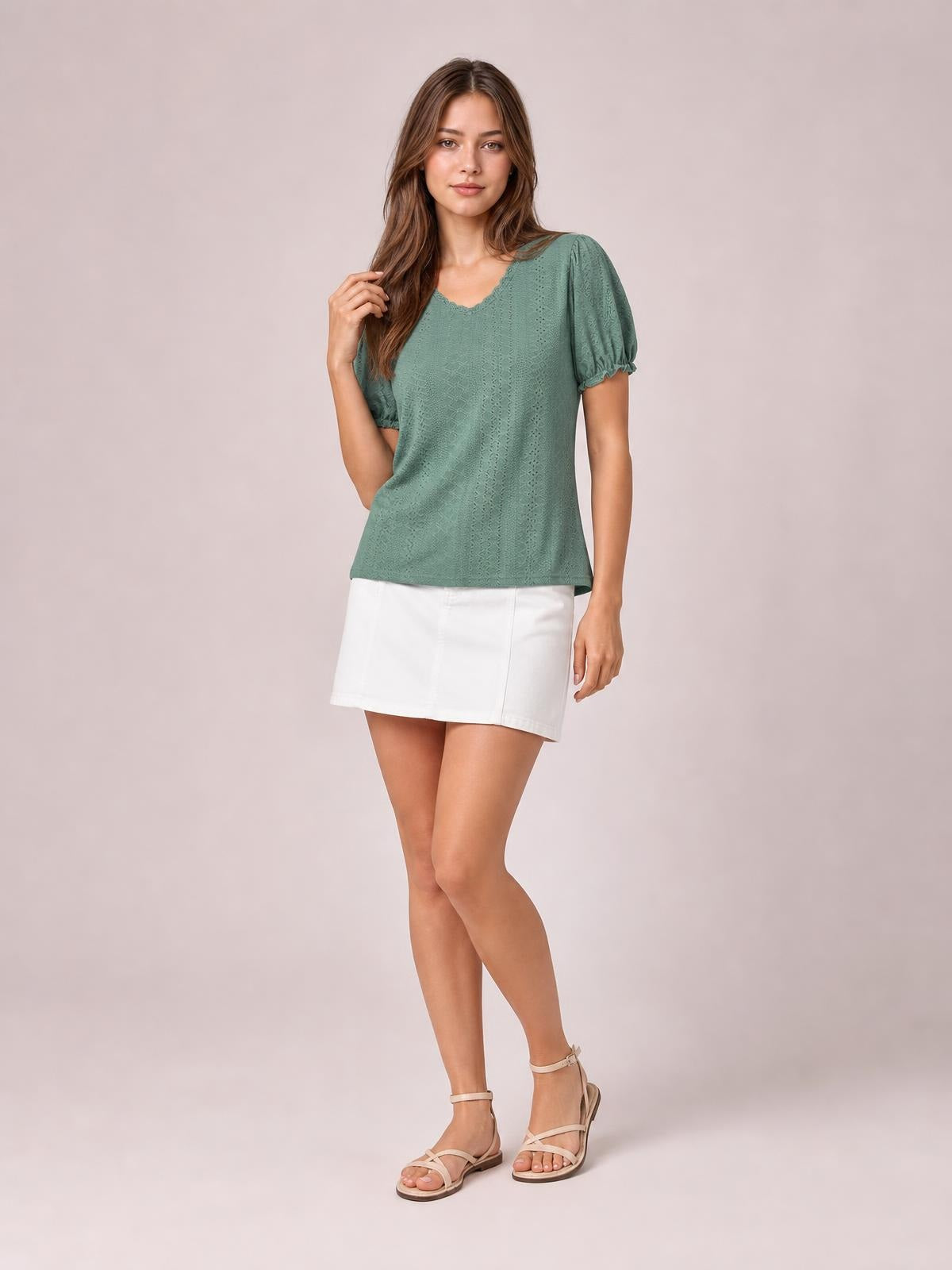 Model poses in a sage green eyelet blouse with a round neckline, delicate frill trim, short puff sleeves, and a relaxed straight silhouette.