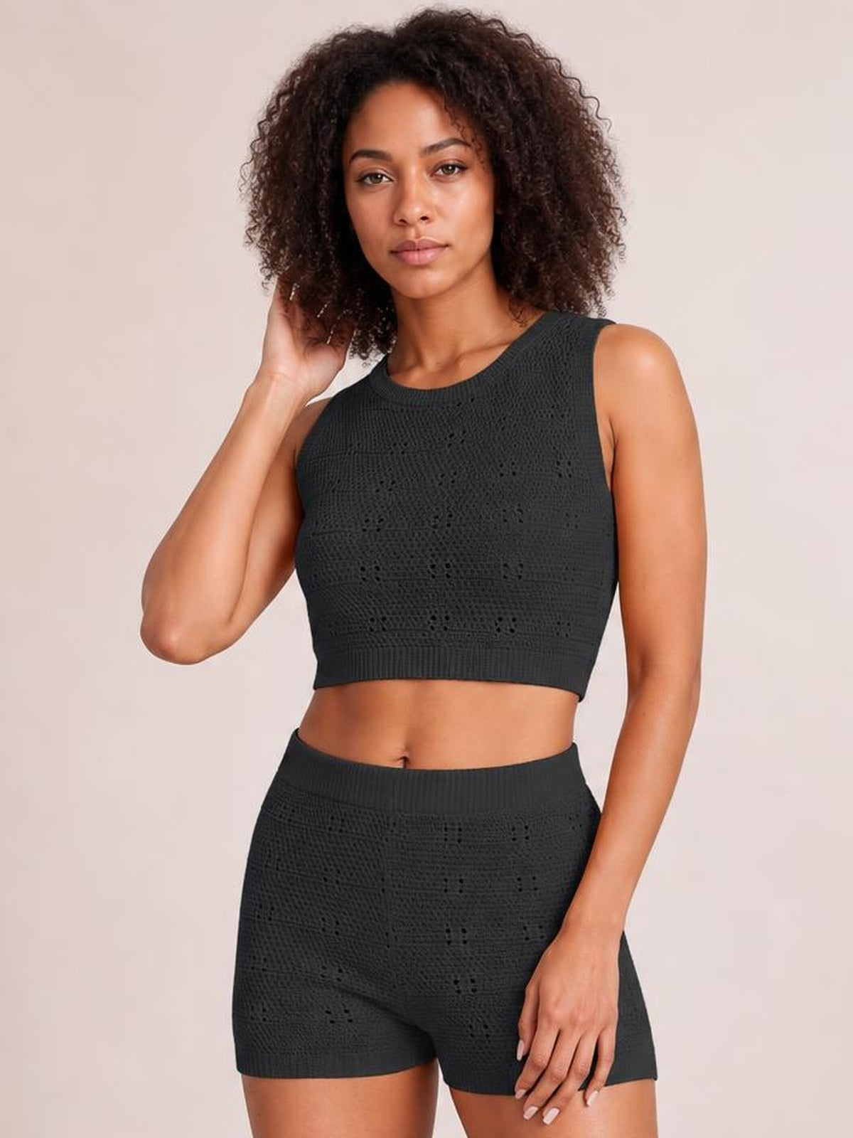 Model wearing a black eyelet round neck tank and shorts sweater set with a cropped fitted silhouette, ribbed edges, and textured openwork knit.