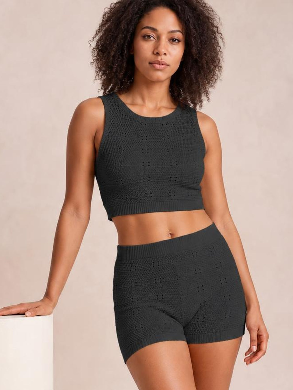 Model in a dark charcoal eyelet sweater set with a round-neck cropped tank and high-waisted shorts, posing with one hand resting at her side.