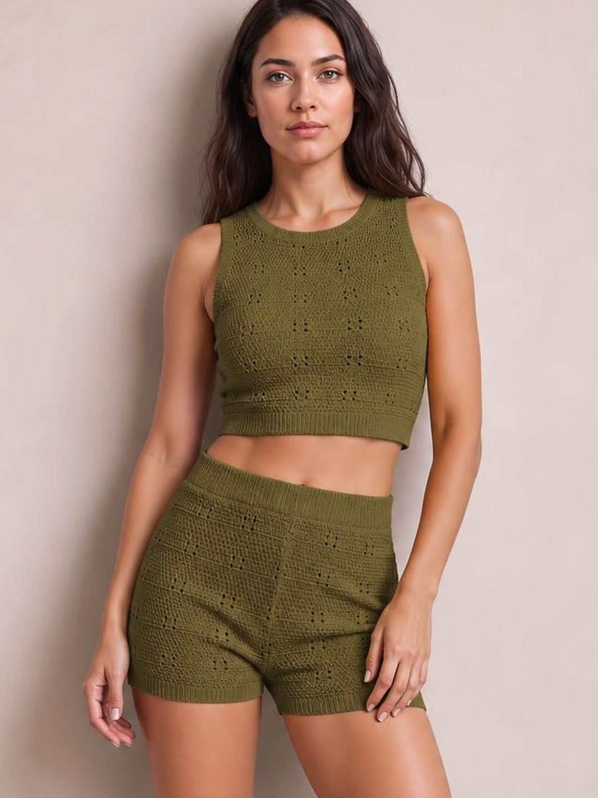 Model poses in an olive green eyelet sweater set with a round neck tank, fitted cropped silhouette, and matching high-waisted shorts with ribbed hems.