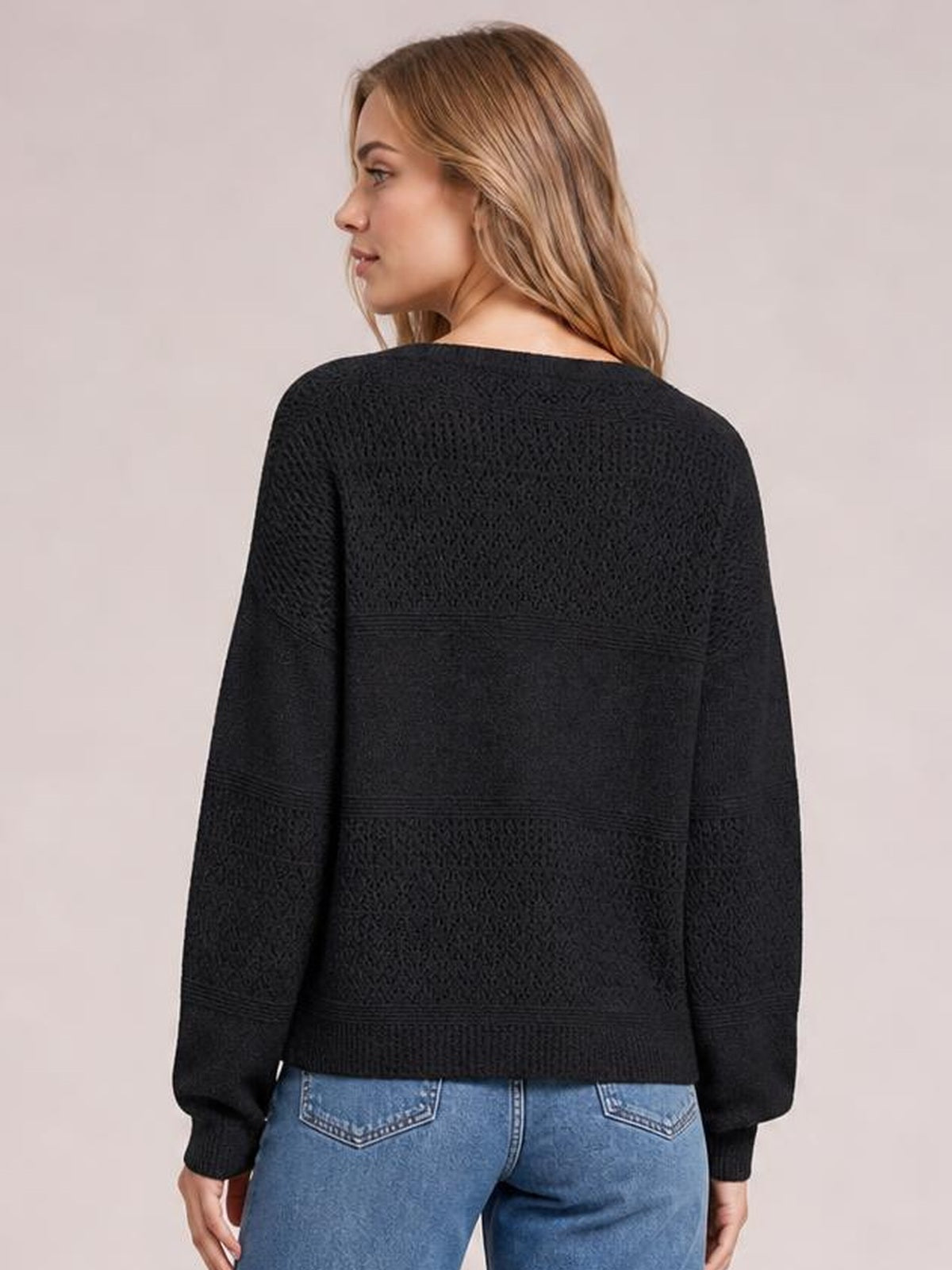 Model shown from behind wearing a black eyelet long-sleeve sweater with a relaxed silhouette, textured knit panels, ribbed cuffs, and a ribbed hem.