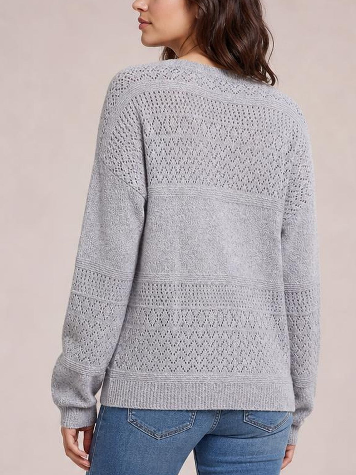 Model shown from behind wearing a light gray eyelet sweater with long sleeves, an openwork knit pattern, relaxed silhouette, and ribbed cuffs and hem.