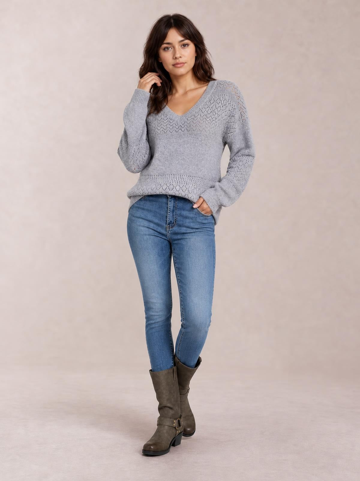 Model poses in a gray eyelet V-neck long sleeve sweater with an easy relaxed silhouette, ribbed cuffs, and horizontal knit detailing.