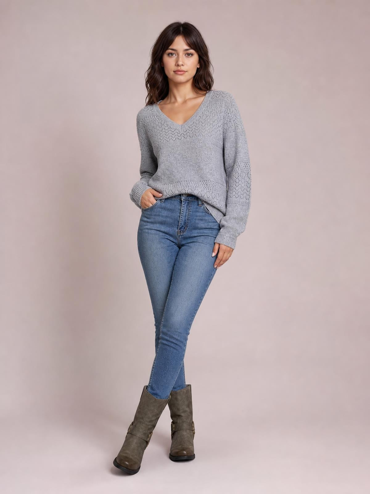 Model in a relaxed pose wears a gray eyelet V-neck long sleeve sweater with a textured knit, ribbed cuffs and hem, and a relaxed silhouette.