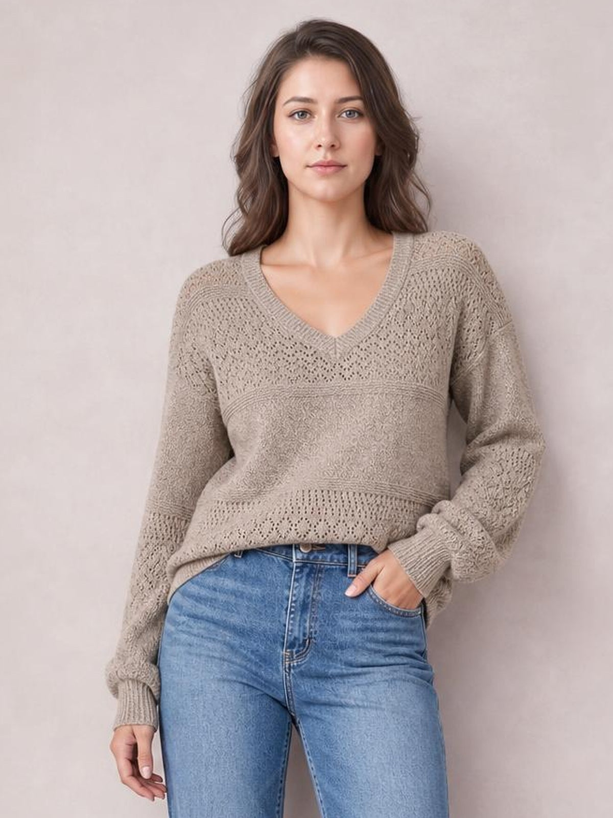 Model wearing a taupe eyelet V-neck long sleeve sweater with a relaxed silhouette, ribbed cuffs and hem, and textured openwork knit panels.
