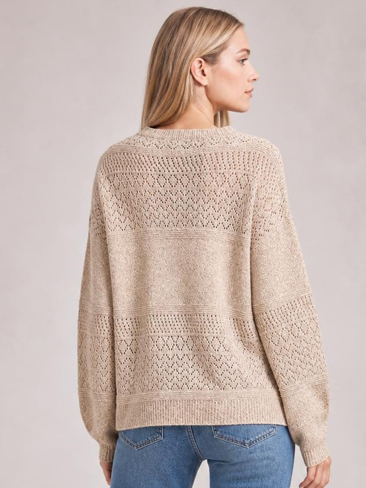 Model shown from the back in a beige eyelet long-sleeve sweater with an openwork knit pattern, relaxed silhouette, and ribbed cuffs and hem.