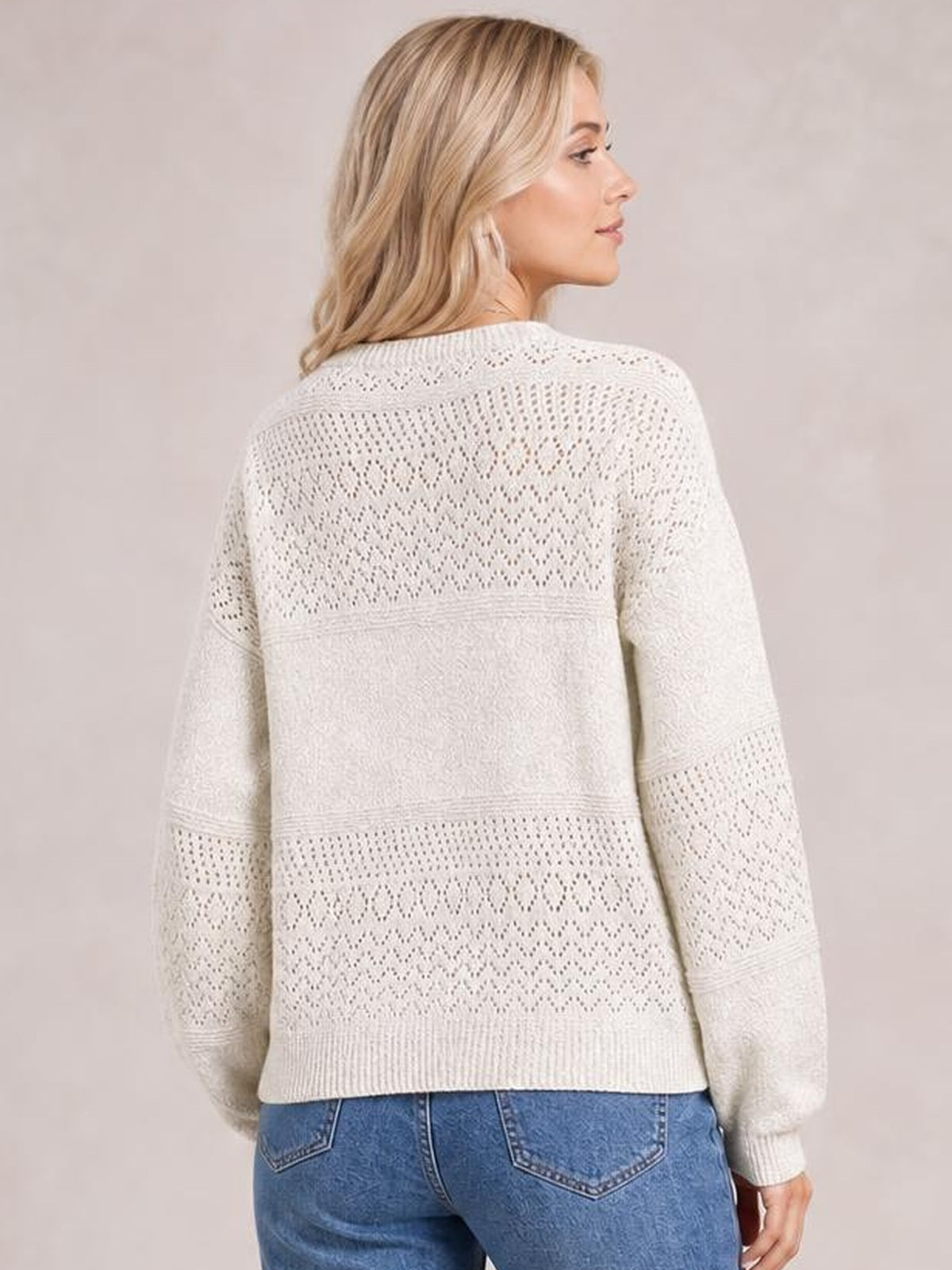 Model shown from the back in a relaxed ivory eyelet sweater with long sleeves, patterned knit panels, ribbed cuffs, and a straight hem.