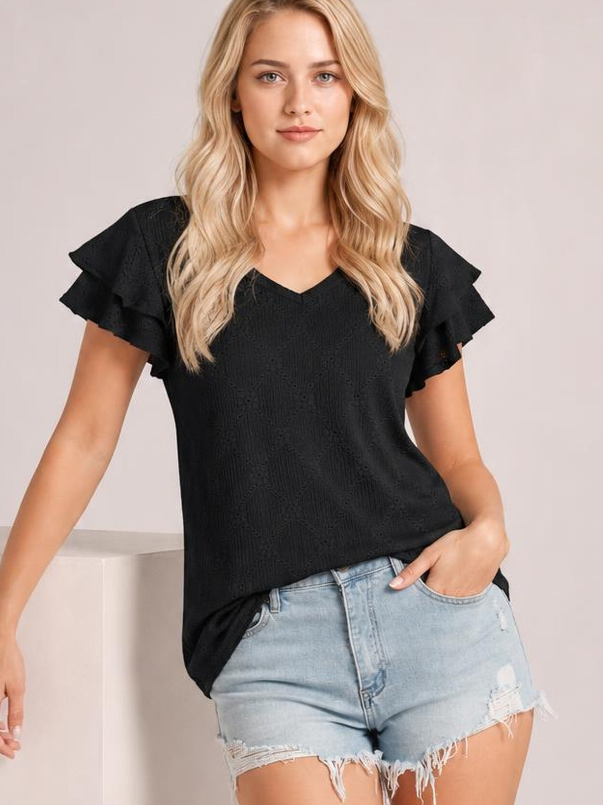 A model poses in a black eyelet V-neck top with layered ruffled cap sleeves and a relaxed straight silhouette.