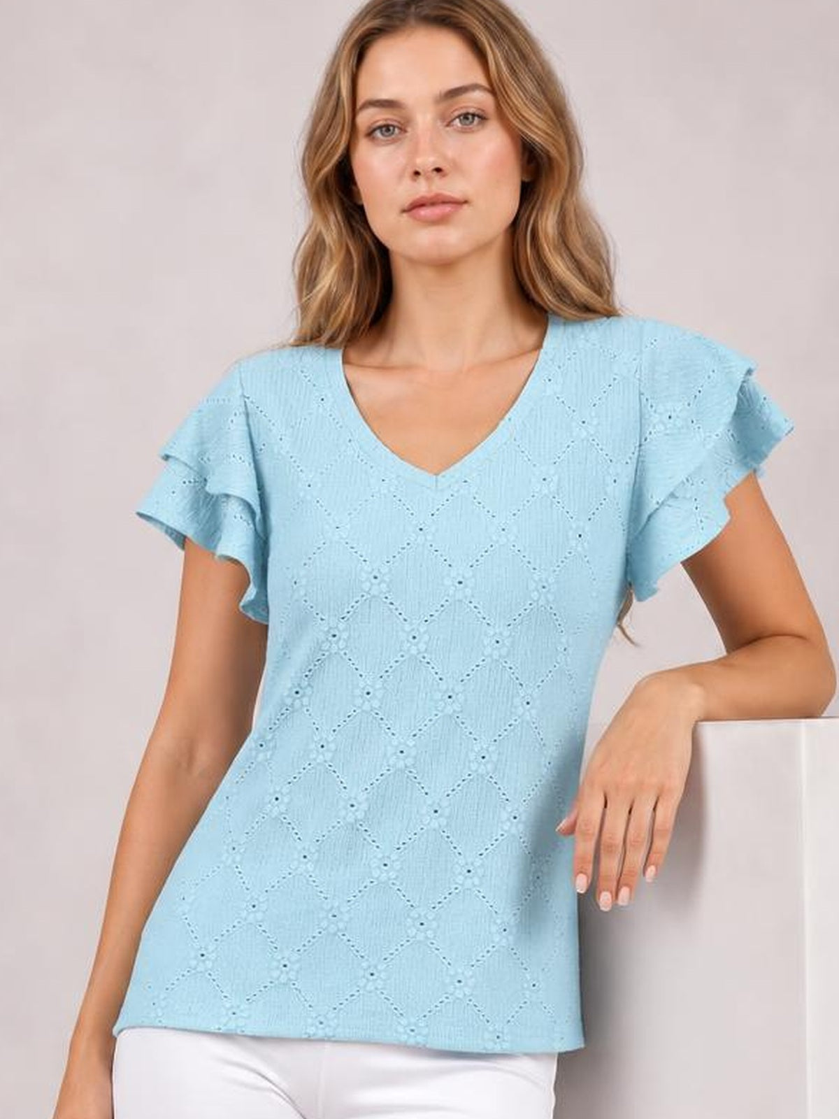Model wears a light blue eyelet top with a V-neck, layered ruffled cap sleeves, lace detailing, and a relaxed straight silhouette.