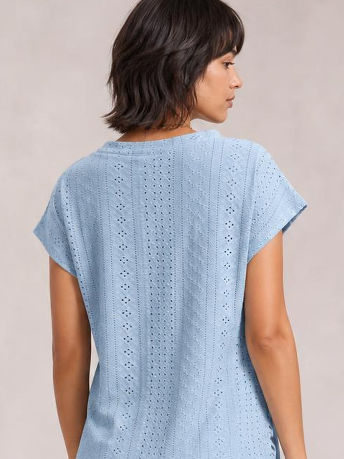 Model shown from behind wearing a light blue eyelet top with short sleeves, vertical openwork detailing, and a relaxed, straight silhouette.