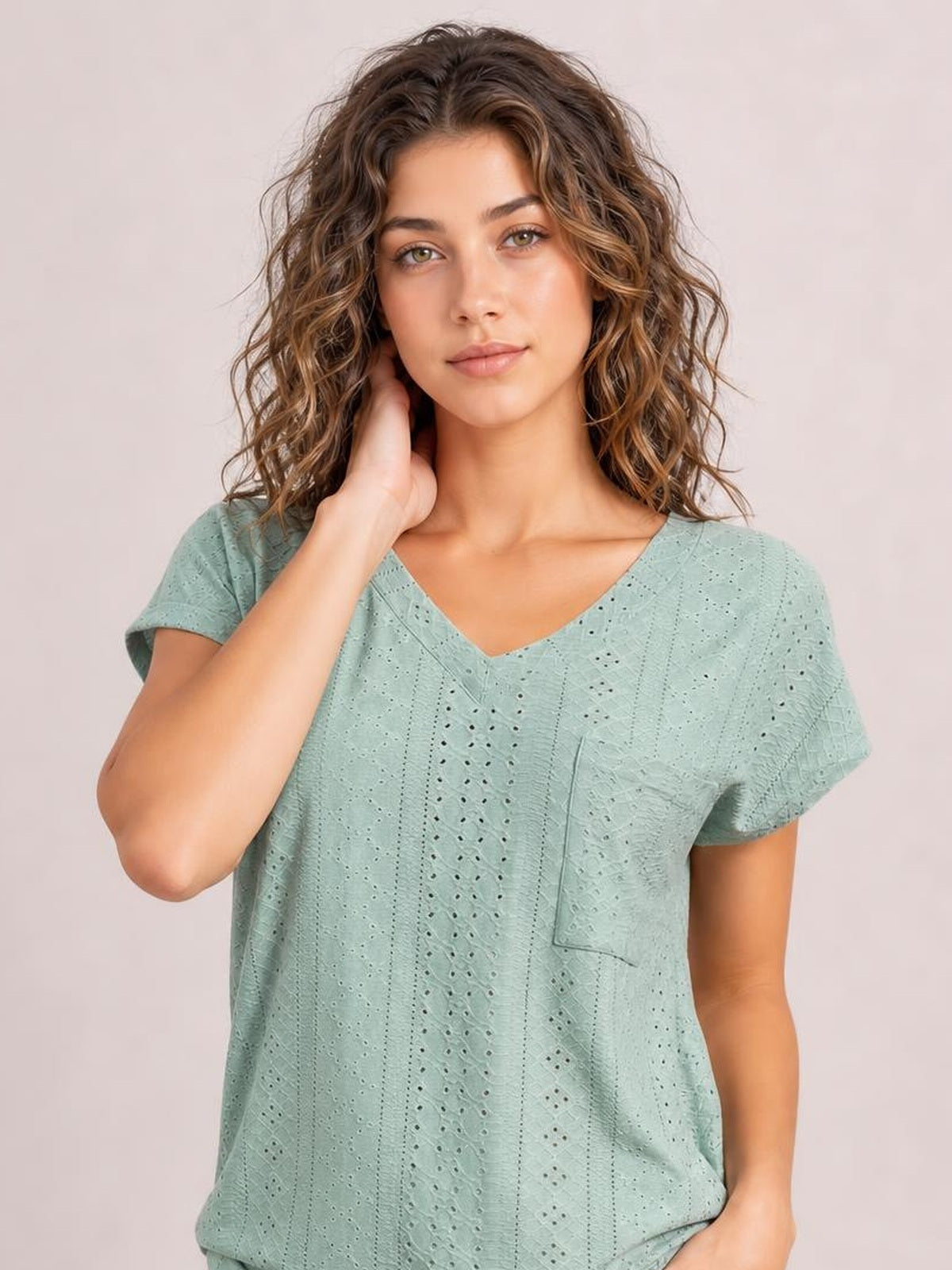A model poses in a mint green eyelet V-neck short sleeve top with a relaxed silhouette, vertical detailing, and a practical patch pocket.