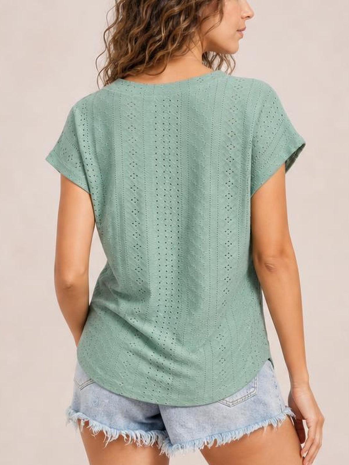 A model wears a mint green eyelet short sleeve top with a relaxed silhouette, softly rounded hem, and vertical openwork construction, shown from the back.