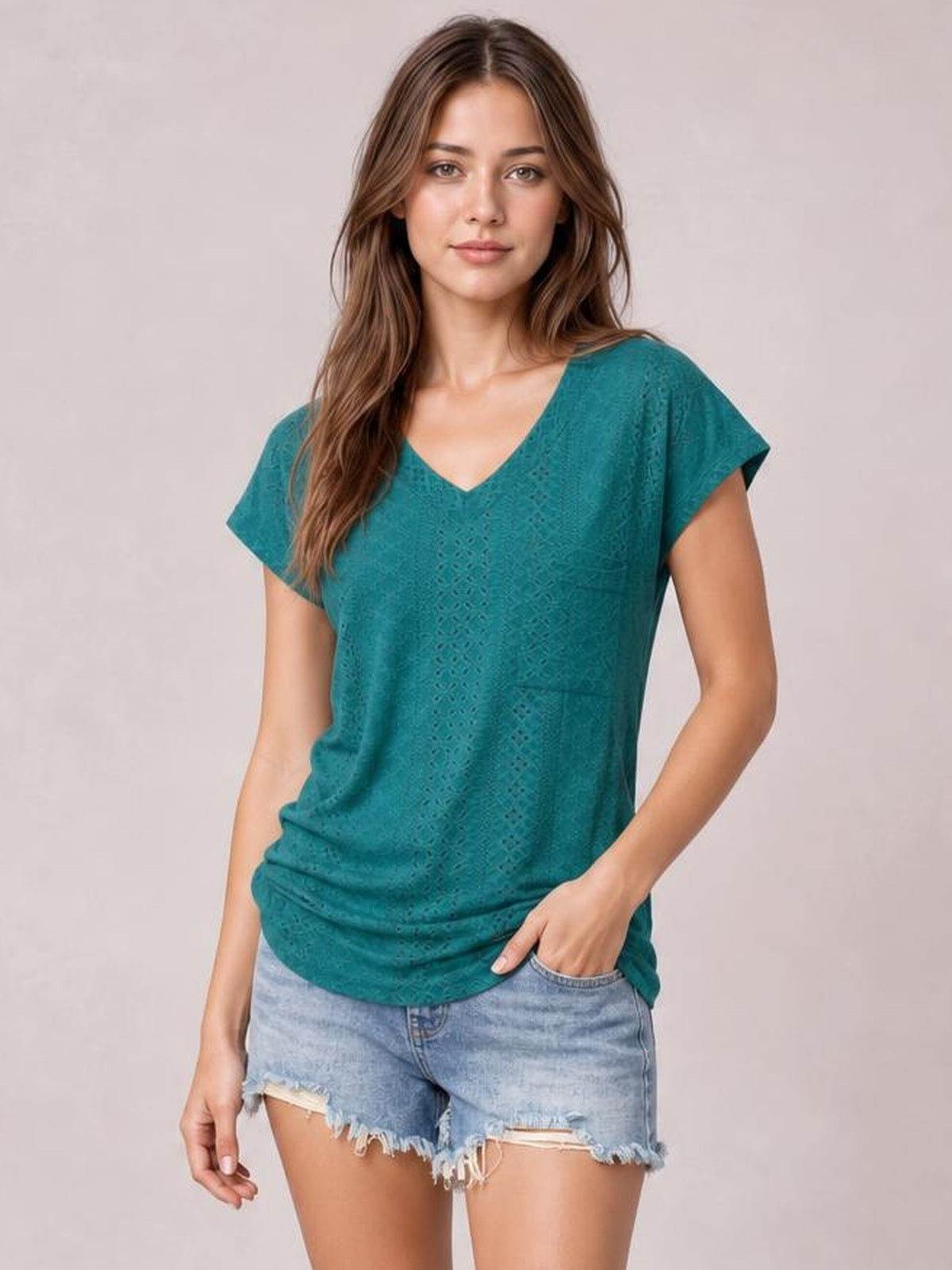 A model poses in a teal eyelet V-neck short sleeve top with a relaxed silhouette, textured openwork construction, and softly draped hem.