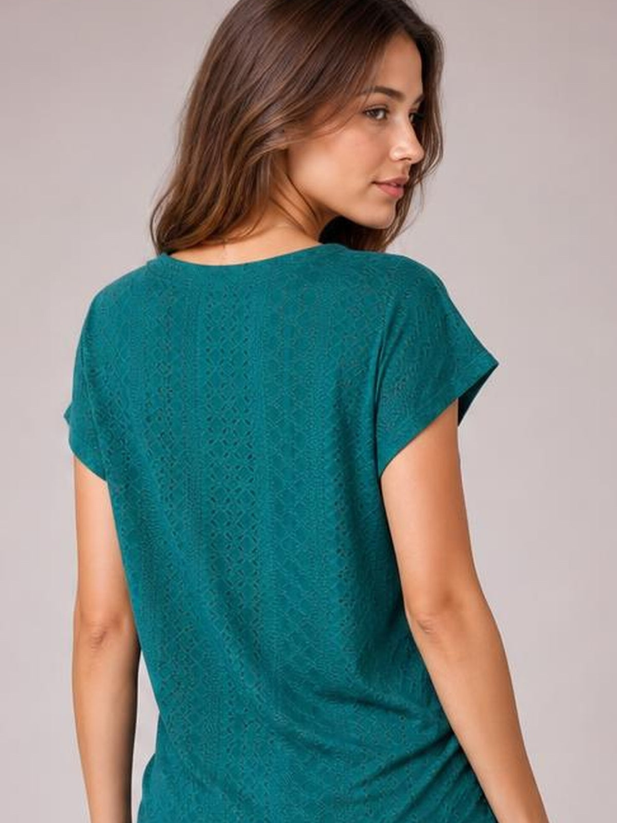A model looks over her shoulder while wearing a teal eyelet short-sleeve top with an allover textured pattern and relaxed, straight silhouette.