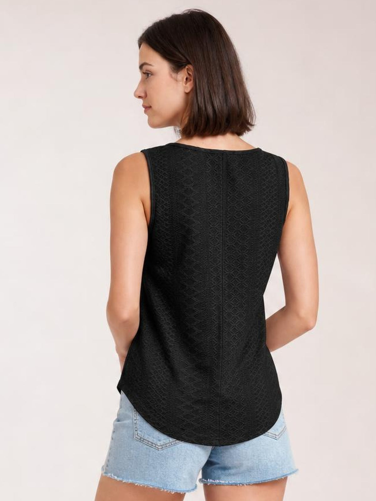 Model shown from the back wearing a black eyelet tank with wide straps, a relaxed silhouette, textured pattern, and a rounded curved hem.
