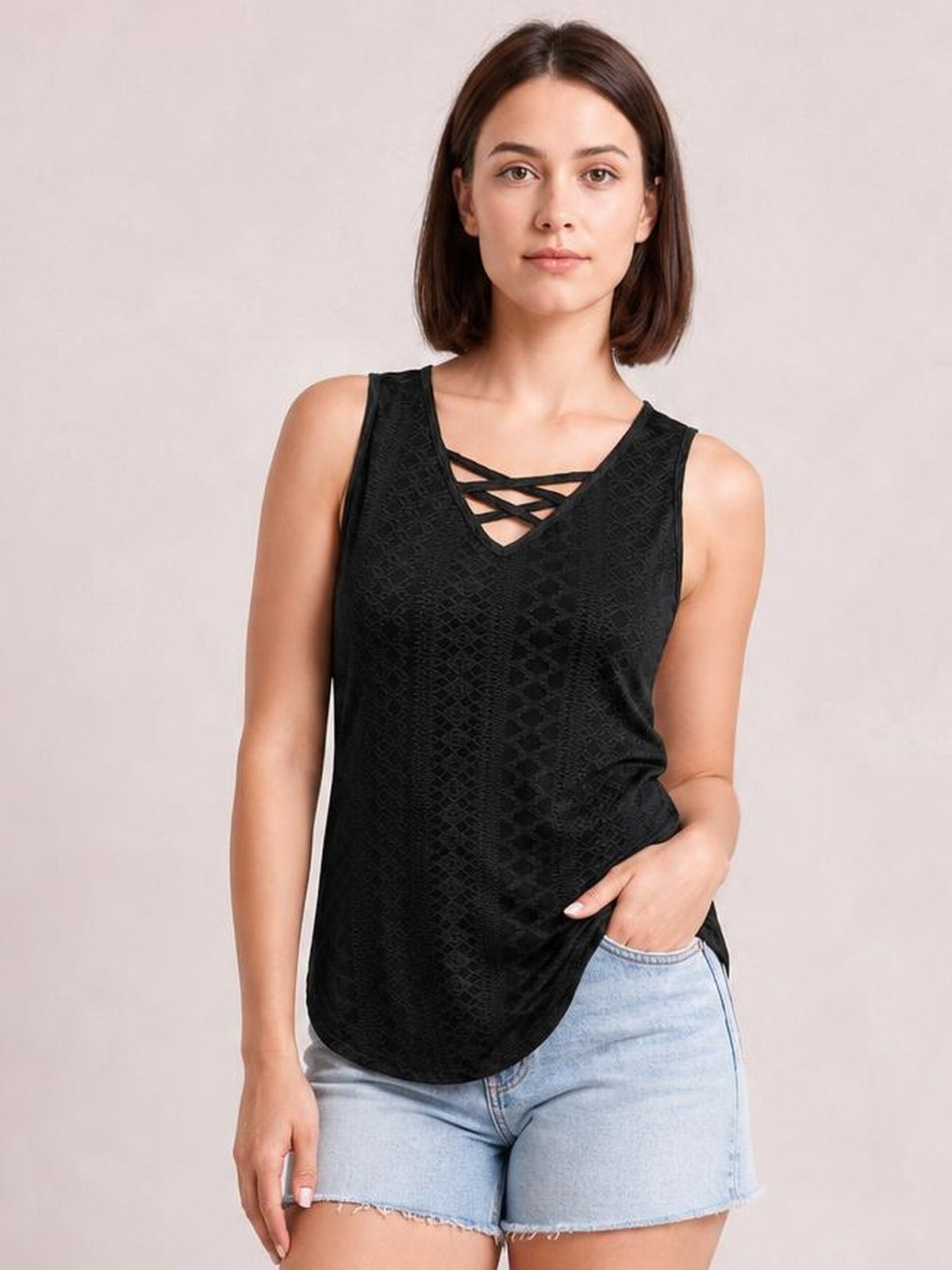 Model poses in a black eyelet wide-strap tank with a crisscross V-neck, sleeveless construction, relaxed silhouette, and curved hem.