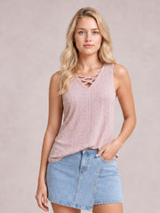 A model poses with one hand in her pocket wearing a dusty pink eyelet tank with wide straps, a relaxed silhouette, and crisscross neckline detail.