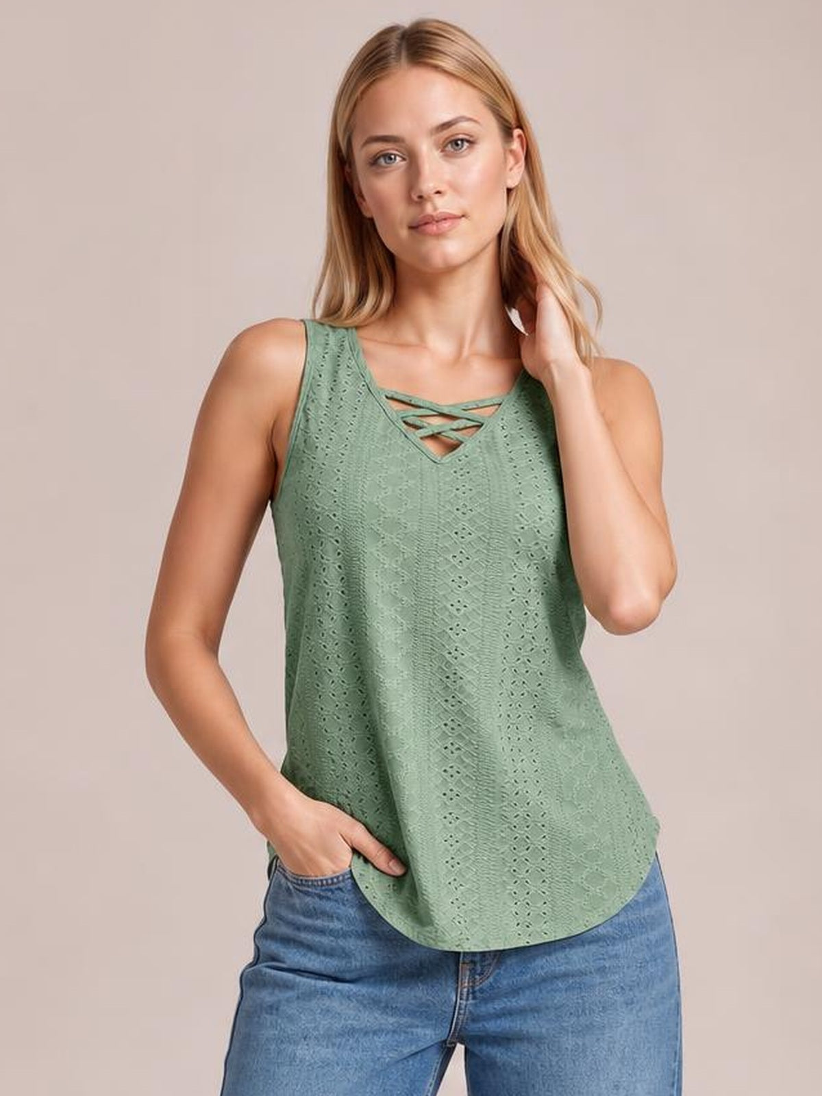 A model poses in a sage green eyelet tank with wide straps, a relaxed curved-hem silhouette, and crisscross lace-up neckline.