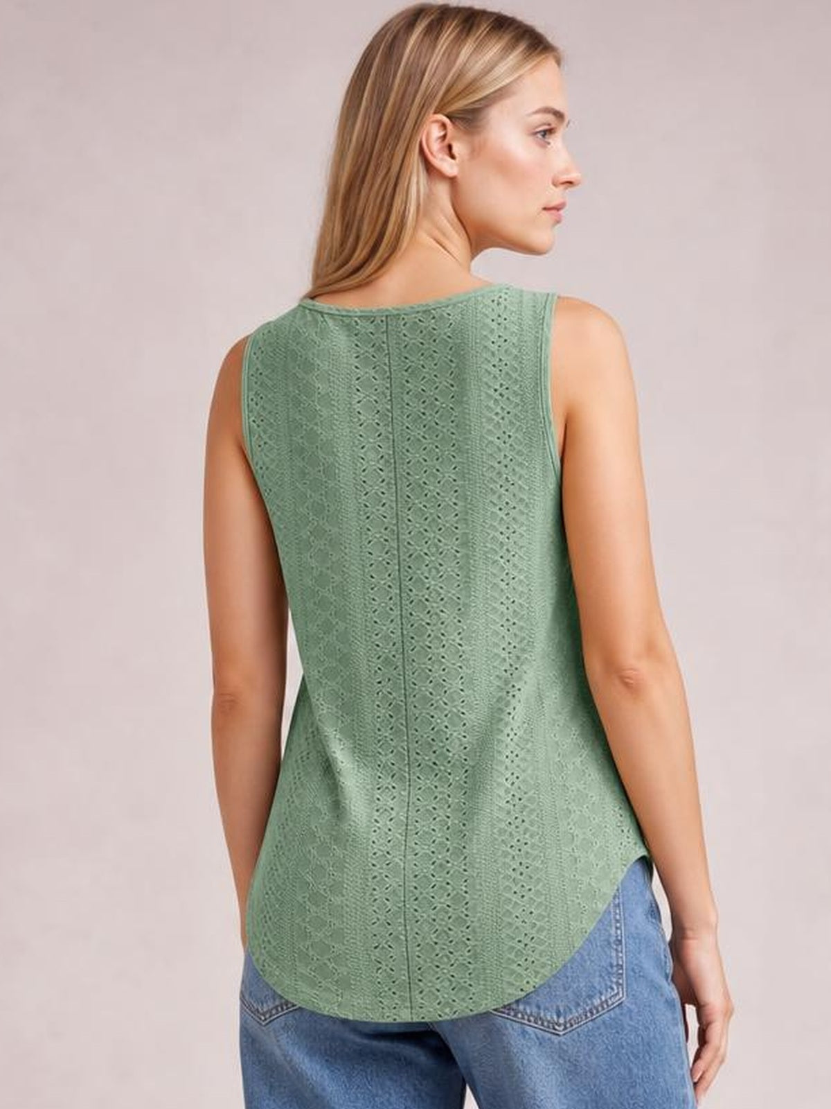 A model turns to show the sage green eyelet wide strap tank’s relaxed silhouette, textured back, wide shoulder straps, and rounded hem.