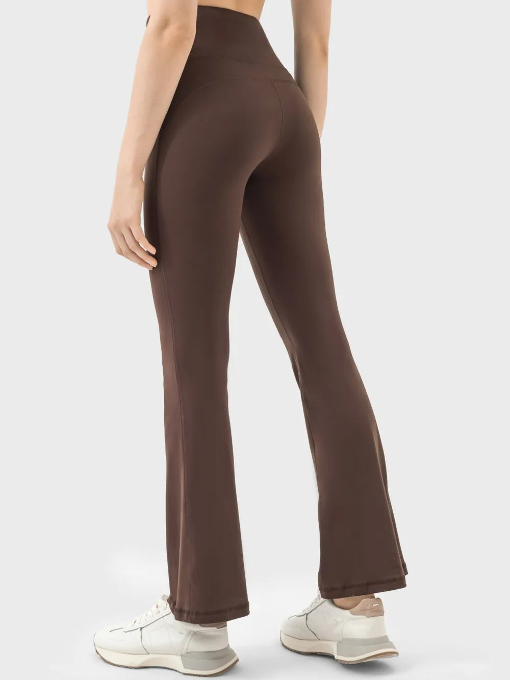 Rear view of a model wearing brown high-waist active pants with a sleek, stretchy fitted silhouette through the hips and thighs and subtly flared legs.
