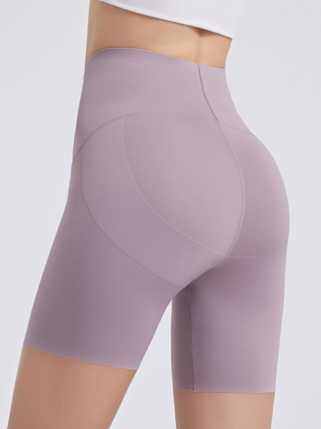 Model shown from the side wearing lilac wide waistband sports shorts with a high-rise, fitted biker-short silhouette and curved panel seams.