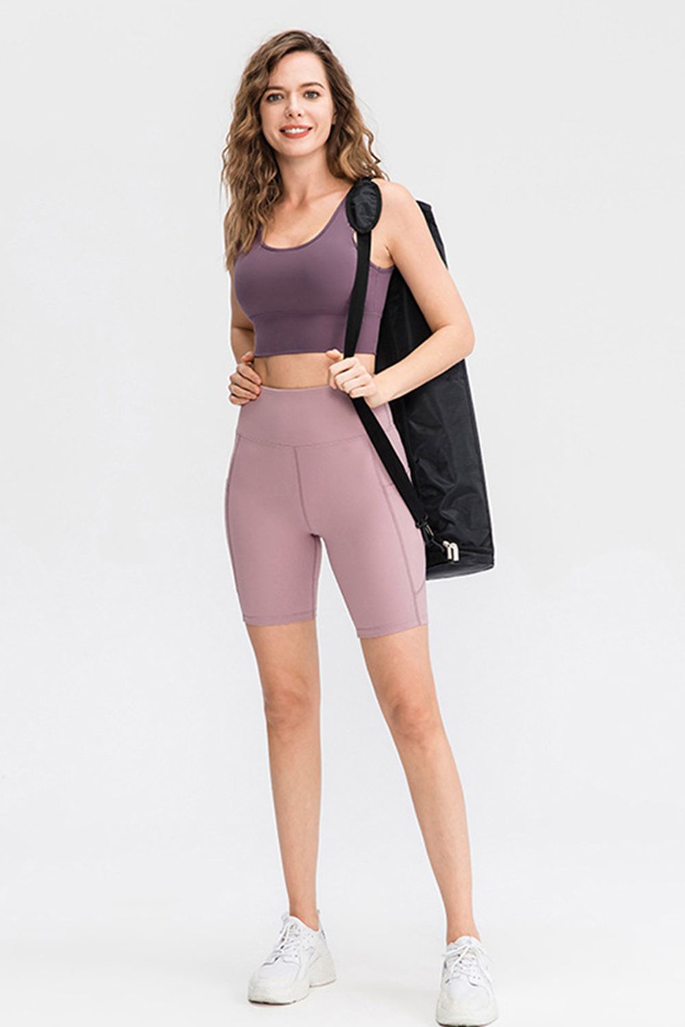 A model wears solid mauve sports shorts with a wide high waistband, fitted stretch silhouette, and knee-length biker-style construction.