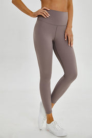 Model poses in taupe sports leggings with a wide seamless band waist, fitted full-length silhouette, and visible front and inner-leg seams.