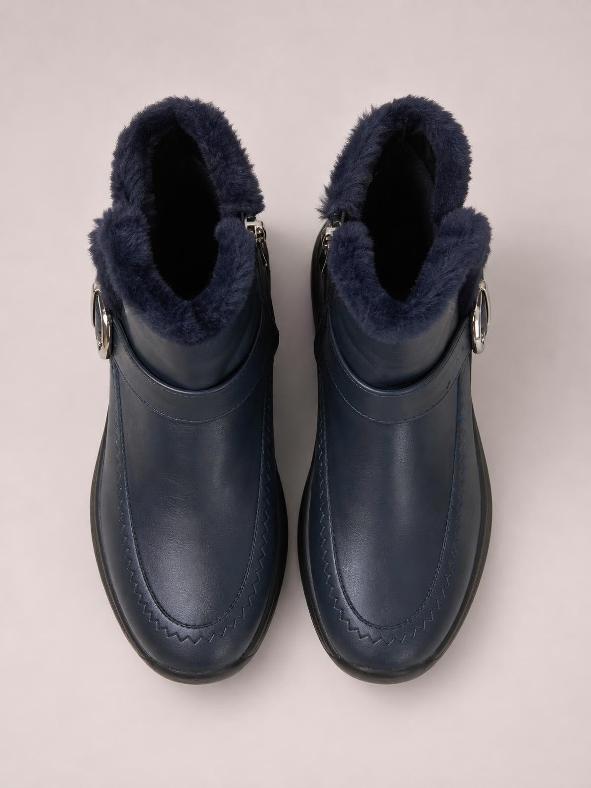Pair of dark navy faux fur lined winter ankle boots with rounded toes, flat rubber soles, stitched panels, and silver side hardware.