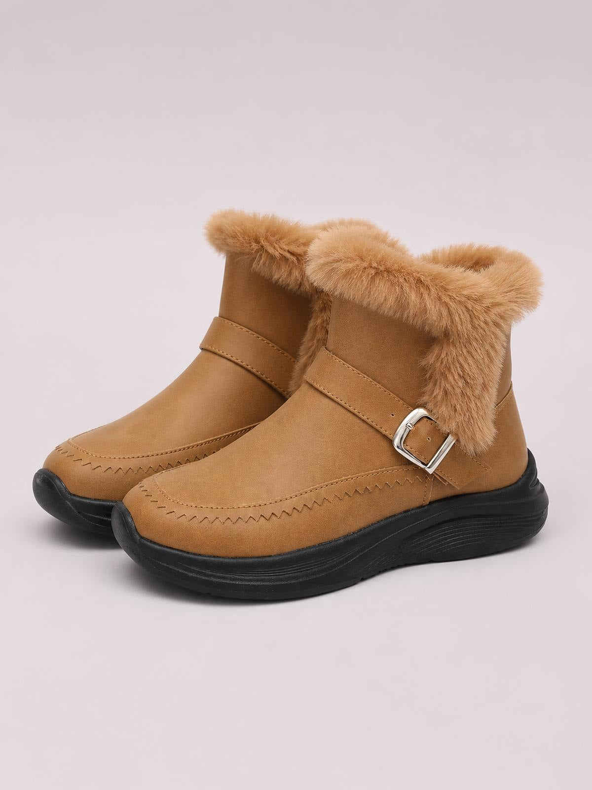 Tan faux fur lined winter ankle boots feature a flat silhouette, buckled side straps, stitched rounded toes, and chunky black rubber soles.