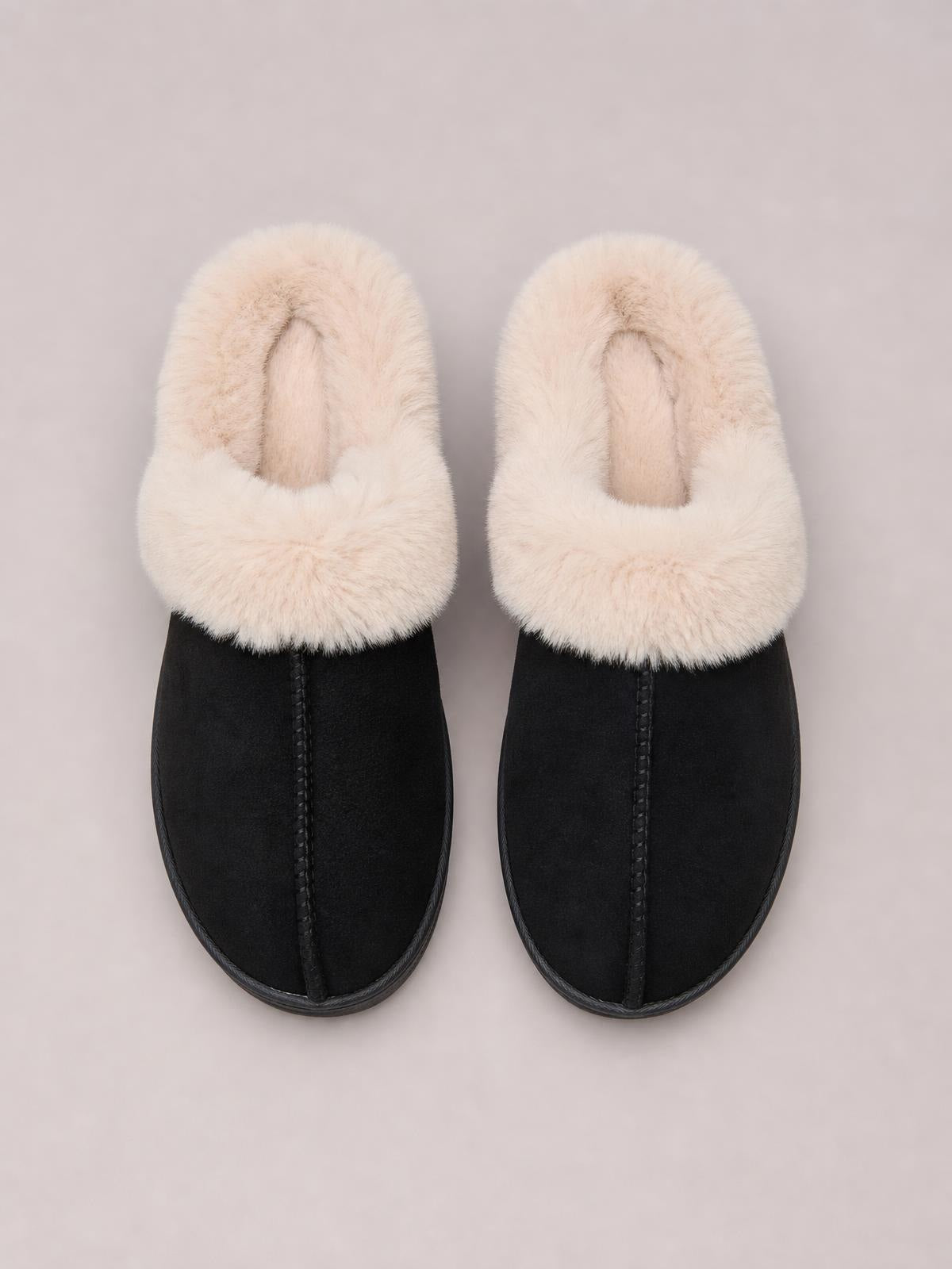 Black round-toe platform slippers with plush cream faux fur lining, suede-like uppers, stitched center seams, and flat rubber soles.