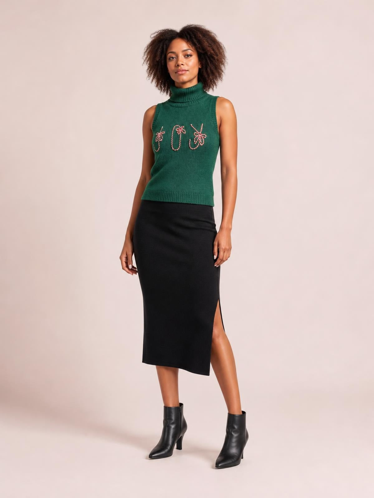 Model poses in a green ribbed turtleneck sweater vest with festive embroidered detailing, sleeveless construction, fitted silhouette, and a straight hem.