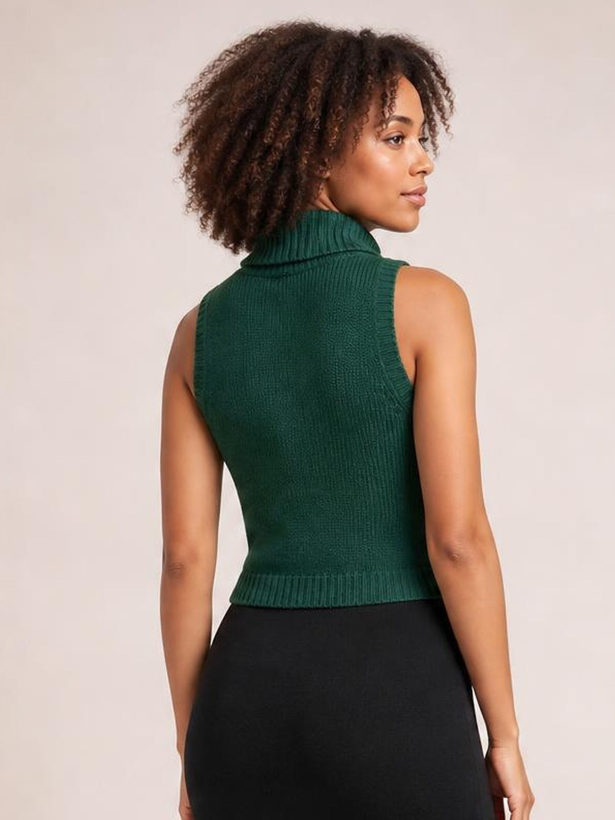 A model shows the back of a dark green ribbed turtleneck sweater vest with a fitted sleeveless silhouette, high collar, and neat hem.