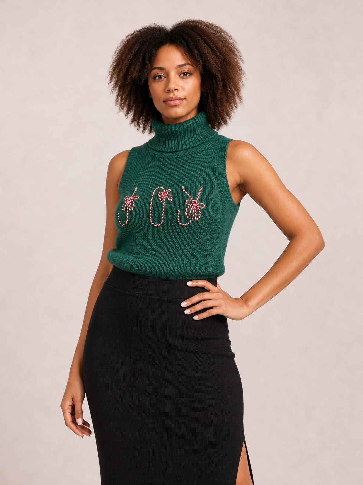 A model poses with one hand on her hip in a green ribbed turtleneck sweater vest featuring festive embroidered candy canes and a fitted sleeveless silhouette.