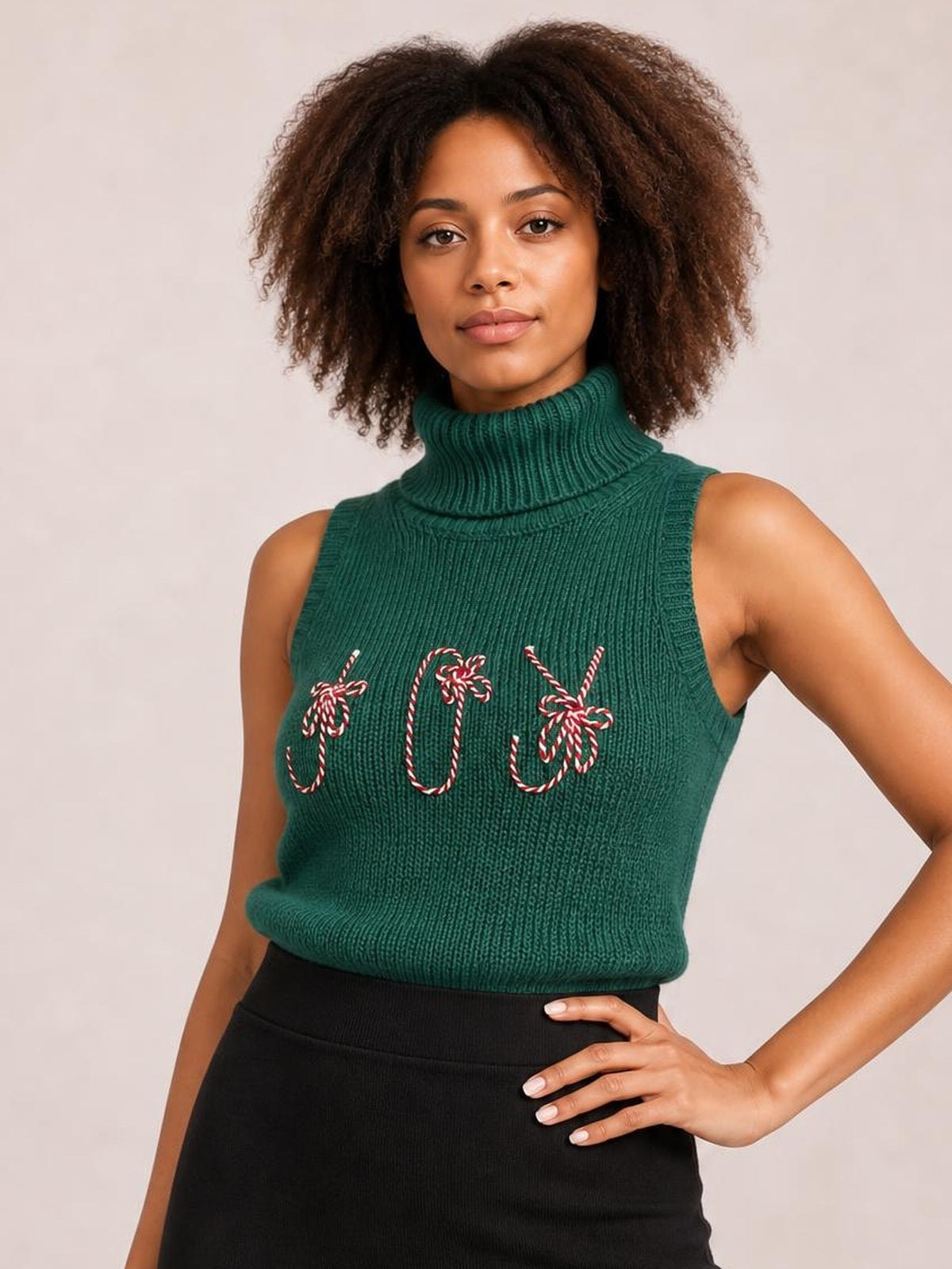 Model poses with one hand on her hip in a green ribbed turtleneck sweater vest featuring a sleeveless silhouette and candy-cane embroidery.