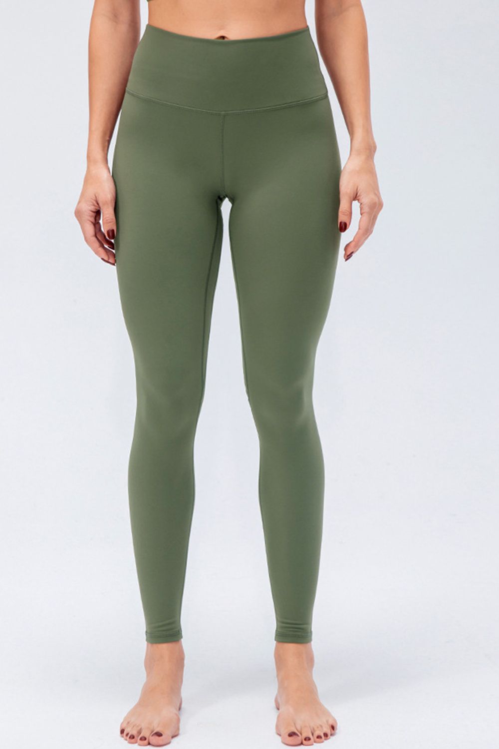 Model wears solid olive-green active leggings with a wide waistband, slim full-length silhouette, and visible center and curved seam construction.