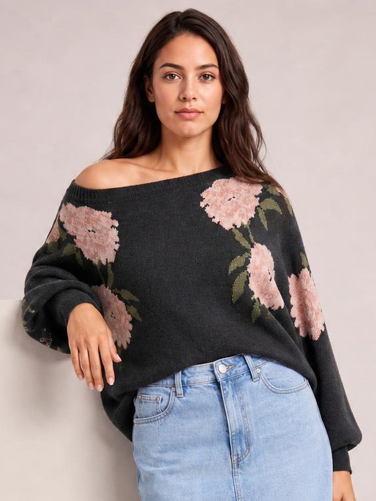 Model wears a black floral boat neck long sleeve sweater with pink flowers, relaxed oversized silhouette, ribbed cuffs, and one shoulder exposed.