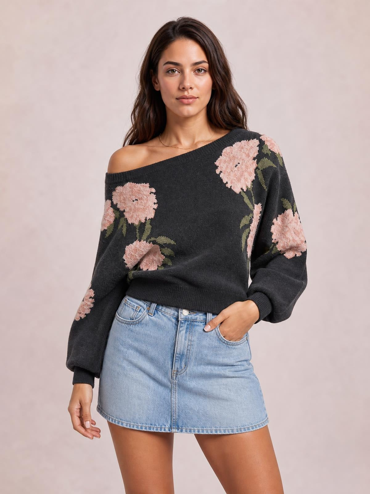 Model poses in a black floral boat neck long sleeve sweater with pink flowers, ribbed cuffs and hem, relaxed sleeves, and a cropped silhouette.