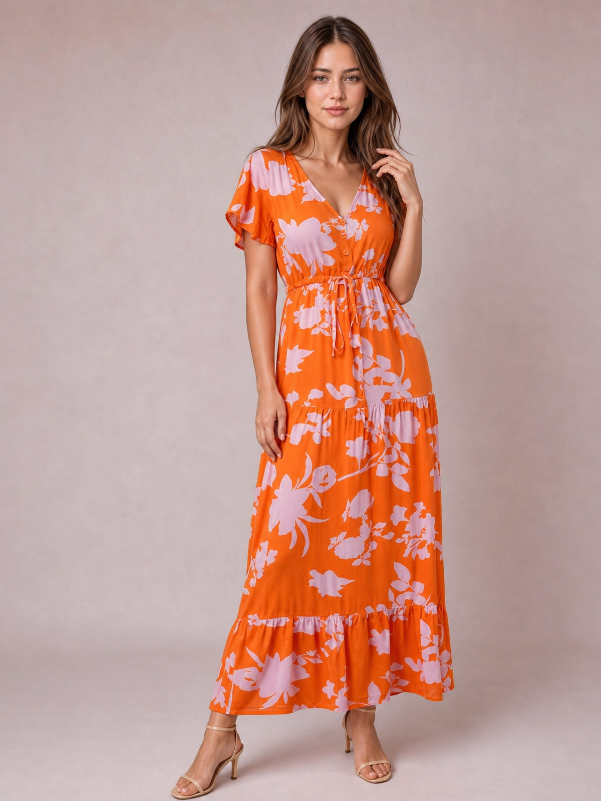 Model poses in an orange floral midi dress with a V-neck, flutter sleeves, buttoned bodice, drawstring waist, and softly tiered skirt.
