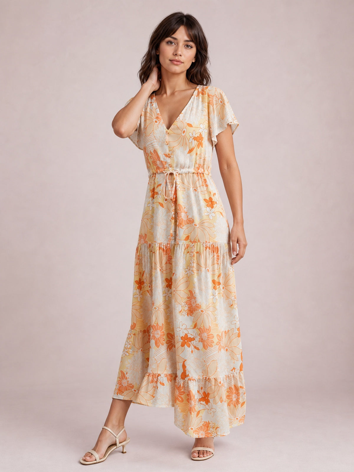 Model poses in a floral midi dress with a V-neck, flutter sleeves, buttoned front, drawstring waist, and softly tiered silhouette in cream and orange.