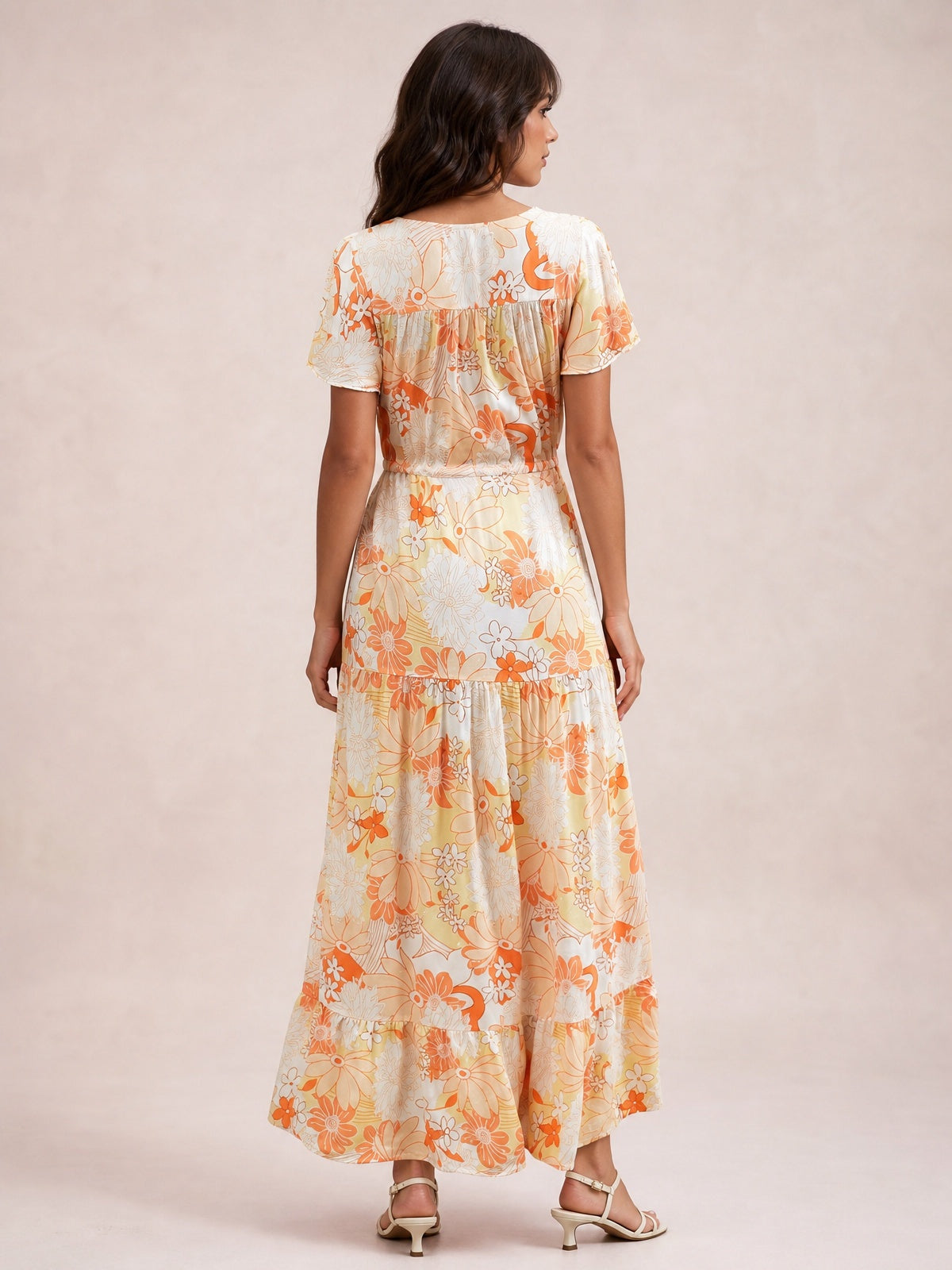 Back view of a model in a cream and orange floral midi dress with short flutter sleeves, a defined waist, and a flowing tiered skirt.