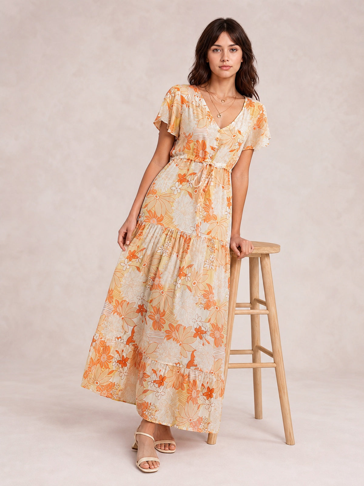 Model poses in an orange and cream floral midi dress with a V-neck, buttoned bodice, flutter sleeves, drawstring waist, and tiered skirt.