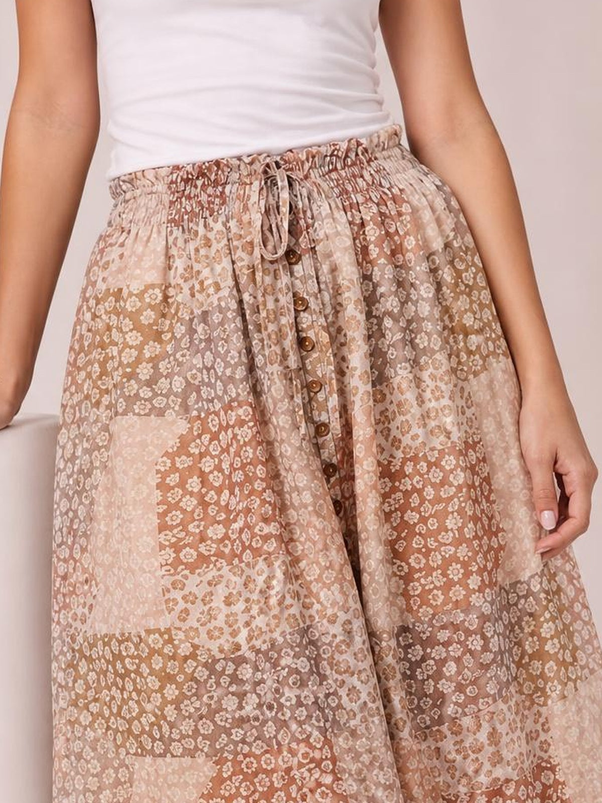 Model displays a flowing boho maxi skirt in beige and brown floral print with an elastic drawstring waist and buttoned front slit.