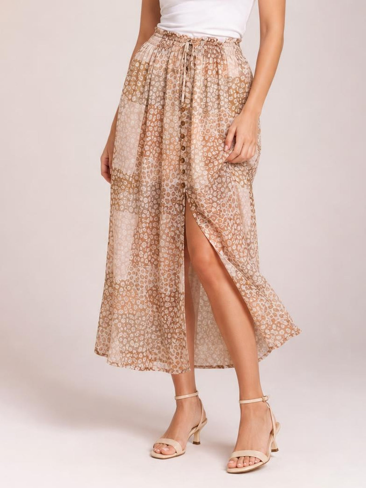 Model wearing a flowing beige floral maxi skirt with a buttoned front, elastic drawstring waist, and high front slit in a relaxed standing pose.