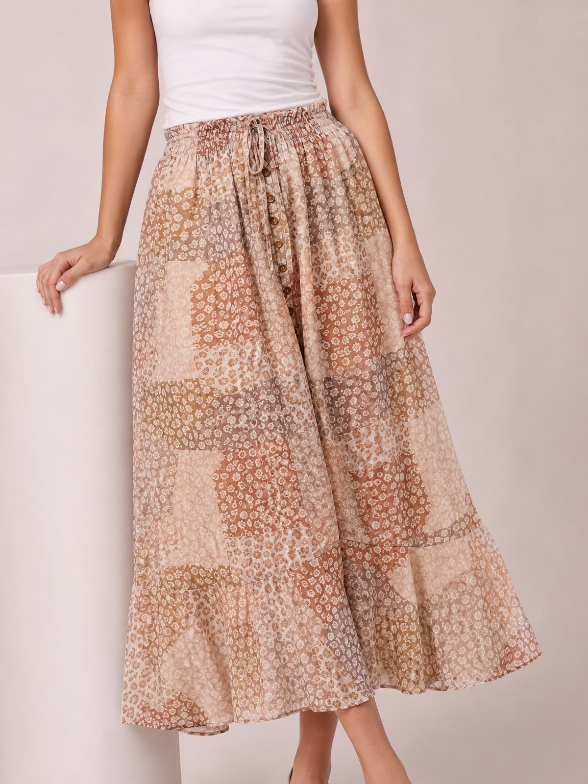 Model wearing a flowing blush and brown floral maxi skirt with a buttoned front, drawstring waist, tiered construction, and relaxed bohemian silhouette.