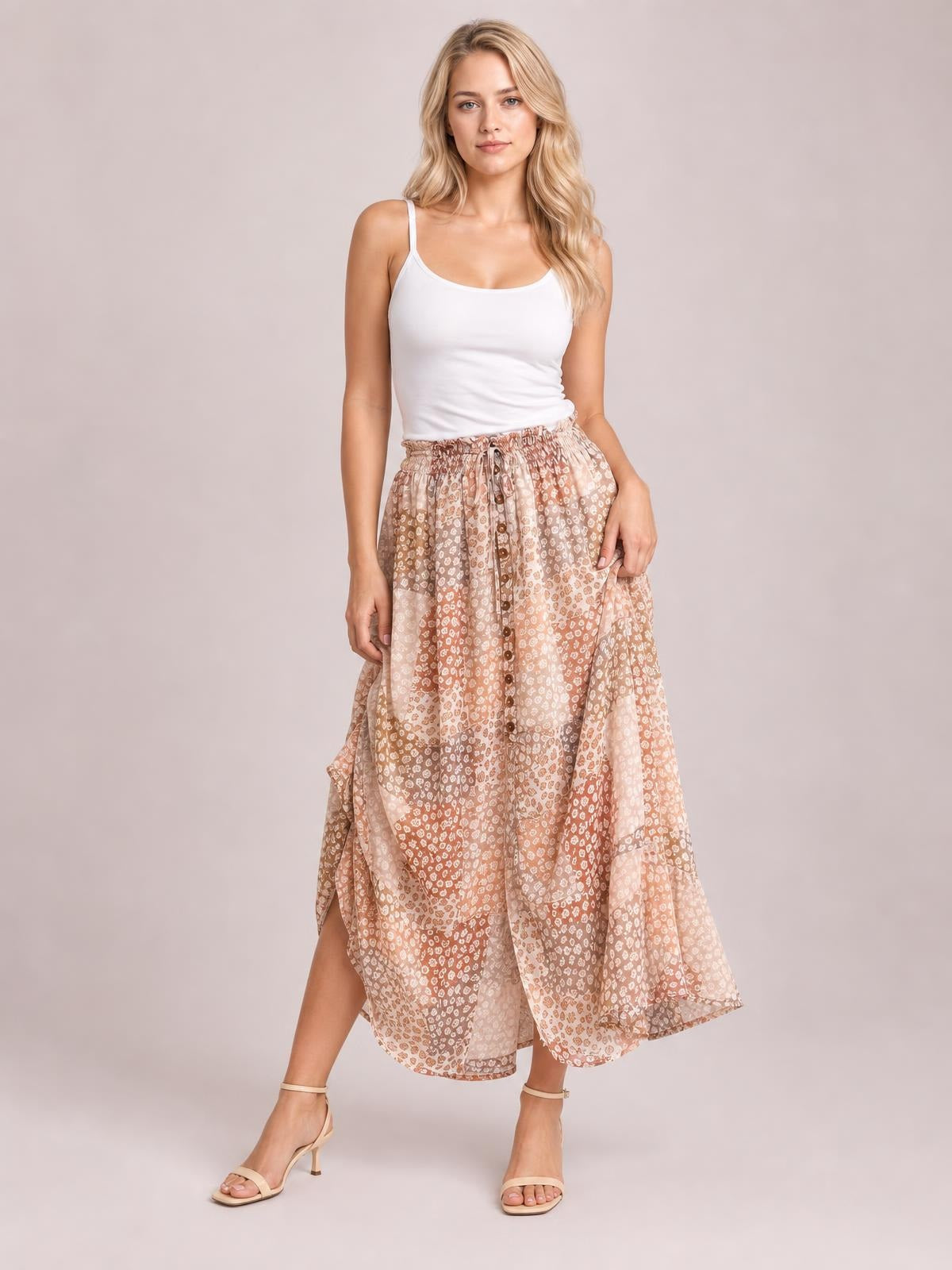 Model wears a flowing peach and taupe floral maxi skirt with a buttoned front, high slit, gathered waist, and airy bohemian silhouette.